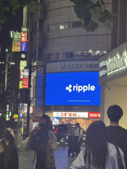 A large digital billboard displays the Ripple logo and name, situated above a SoftBank storefront in the bustling Roppongi district of Tokyo. This image perfectly captures the "Ripple right in the heart of Roppongi" as described.