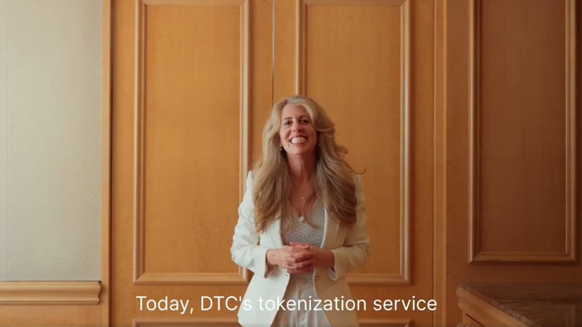 In this image, there's a woman wearing a white blazer standing against a wooden wall with a gold paneling design. She has blonde hair and is smiling at the camera. The text above her reads "Today, DTC's tokenization service", indicating that she is promoting a new service or product related to tokenization.