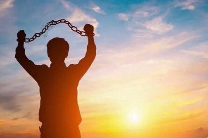A silhouetted figure stands triumphantly against a sunset sky, arms raised while breaking free from chains, symbolizing liberation.