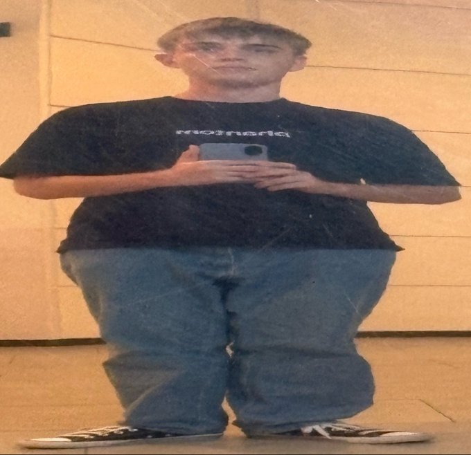 Distorted photo of a person wearing a black t-shirt with 'motnerled' text and baggy jeans, appearing warped or stretched horizontally in a surreal manner.