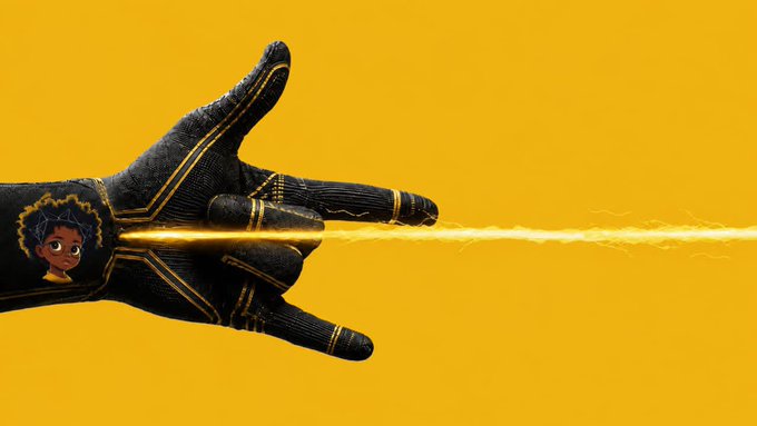 A black and gold gloved hand forming a gun gesture with a yellow energy beam shooting out, featuring a small cartoon character decal on the wrist, against a yellow background.