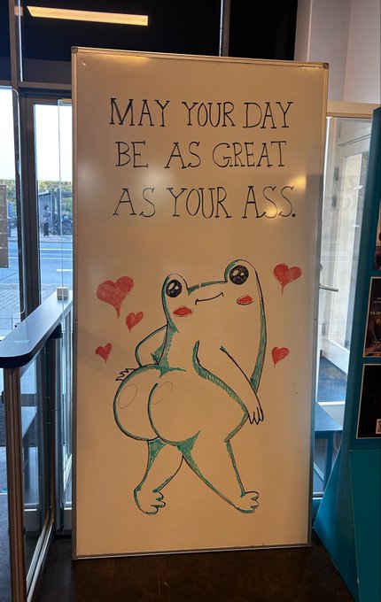 A whiteboard displays the message 'MAY YOUR DAY BE AS GREAT AS YOUR ASS' above a drawing of a frog character surrounded by hearts.