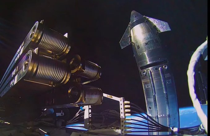 A close-up view of a SpaceX Starship rocket stage attached to its engines and fins against a dark background.