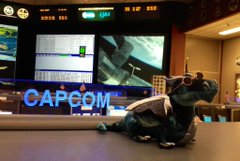 A vinyl figure of a dinosaur-like character lounging in front of a monitor displaying a 'CAPCOM' logo on screen.