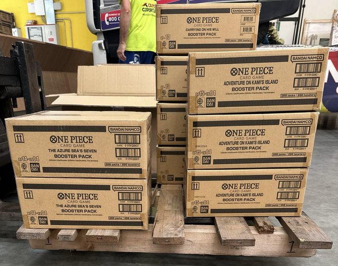 Ten sealed cases of One Piece Card Game booster packs—four cases of "The Azure Sea's Seven" (OP13), three cases of "Carrying On His Will" (OP14), and three cases of "Adventure on Kami's Island" (OP15)—sit stacked on a wooden pallet, representing a $40k delivery ready to be ripped open.