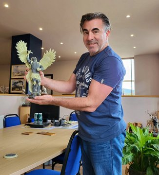 A man proudly holds up a bronze-cast Bitcoin Angel sculpture with outstretched wings, showcasing the 7 kg artwork from his 2024 Archangel Collection as referenced in the accompanying post.