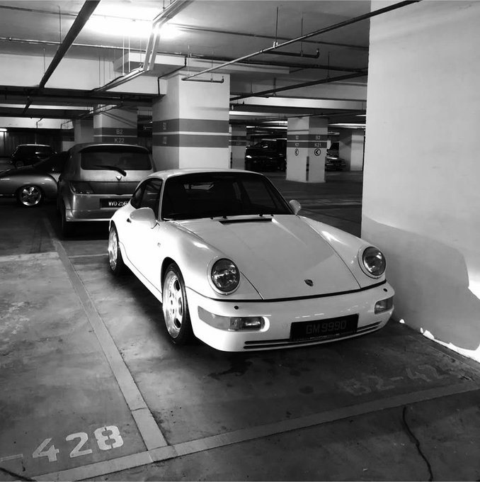 A black and white photo of a white Porsche 911 (license plate GM 9990) parked in an underground garage at spot 428.