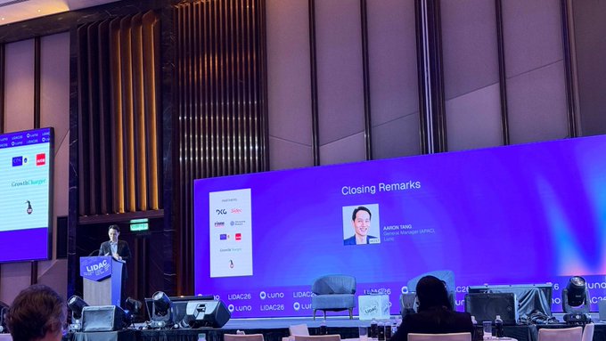 Conference presentation at a UADC event showing a speaker at a podium on stage with a large screen displaying 'Closing Remarks' featuring a portrait of 'JASON YAMO, VP, GLOBAL BUSINESS GROUP'.