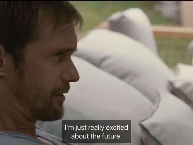 A man with short brown hair and a beard is shown in profile, sitting outdoors on a couch with gray cushions, with the subtitle "I'm just really excited about the future." displayed below him.