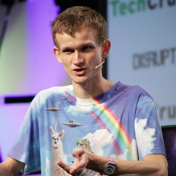 A young man with short brown hair and a headset microphone speaks at what appears to be a TechCrunch Disrupt event, wearing a colorful t-shirt featuring a llama, rainbow, and UFOs.