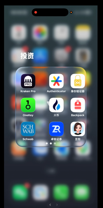 An iPhone home screen shows a folder of finance and crypto apps including Kraken Pro, Authenticator, OneKey, Schwab, and others under the Chinese header '投资' (Investment).