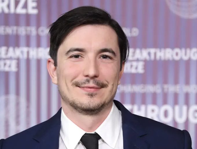 A man with dark hair, a mustache, and a light beard, wearing a navy suit and dark tie, stands on a red carpet with a backdrop reading "BREAKTHROUGH PRIZE." Though the post references Robinhood CEO Vlad Tenev, the person pictured does not clearly match that description.