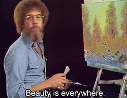 The image features a man with a beard holding a paintbrush, standing next to an easel that has a painting of trees on it. The caption below the image reads "Beauty is everywhere." This message seems to be related to the painting or the artist's work in some way.