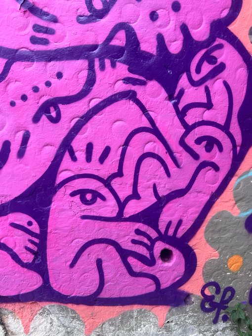 A close-up of pink and purple graffiti street art featuring abstract face designs on a textured wall.