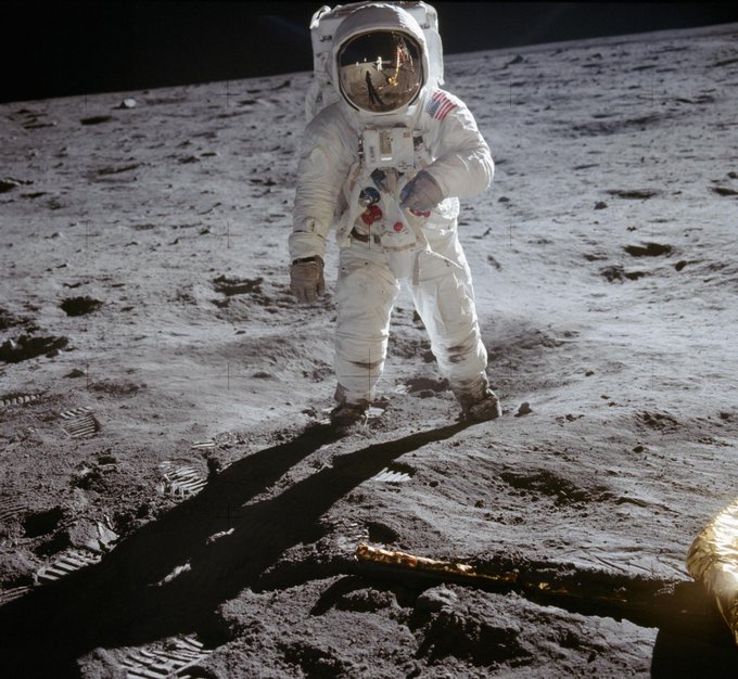An astronaut stands on the dusty surface of the moon, casting a long shadow. This image visually represents the phrase "MOON THAT" by showing one of humanity's most iconic achievements: walking on the moon.