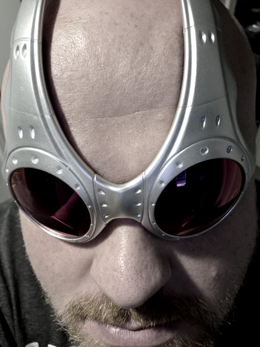Close-up selfie of a person wearing futuristic silver-rimmed goggles with dark lenses, showing their forehead, nose, mustache, and goatee.