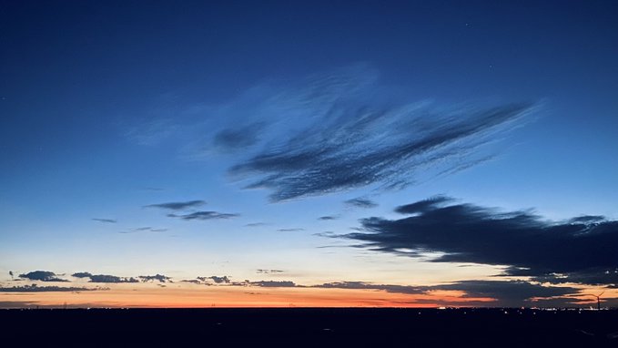 A twilight sky transitioning from deep blue to orange at the horizon with scattered clouds over a dark silhouetted landscape.