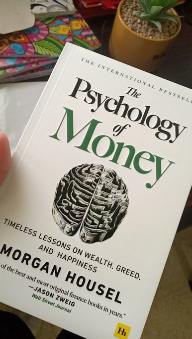 A hand holds the international bestseller book "The Psychology of Money: Timeless Lessons on Wealth, Greed, and Happiness" by Morgan Housel.