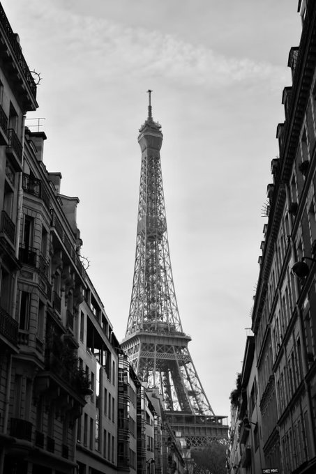 A black and white photograph of the Eiffel Tower in Paris, framed by Parisian buildings on either side.
