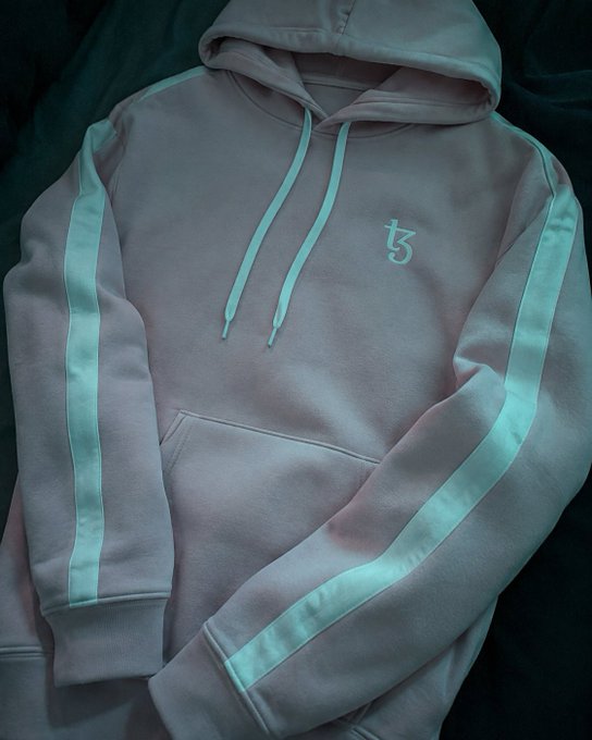 A pink hoodie laid flat on a dark surface, featuring light blue drawstrings, matching side stripes on the sleeves, and a small stylized "ち" logo on the chest.