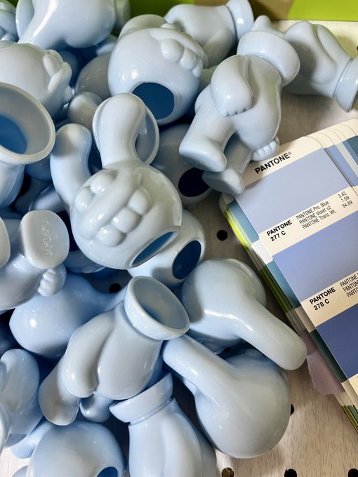 A pile of pale blue ceramic figurines in various shapes rests next to a Pantone color swatch fan showing shades of blue (271 C, 278 C, etc.).
