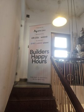Indoor staircase area with a promotional banner advertising "Builders Happy Hours" sponsored by AvanteCAD, LISA unwind, DAT, and Sunset, taking place at City View, Bay City.