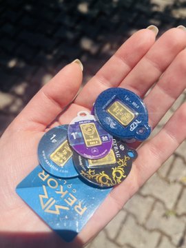 The image shows a hand holding several small, colorful keys or tags with gold-colored designs. These keys are likely used for identification purposes, such as opening doors or accessing certain areas. The text "I need more AURA!!!" suggests that there might be an issue related to these keys and the person is seeking assistance in obtaining additional keys or information about them.

The image also contains a small portion of a brick wall, which could potentially be part of a building's exterior or a decorative element within a space.
