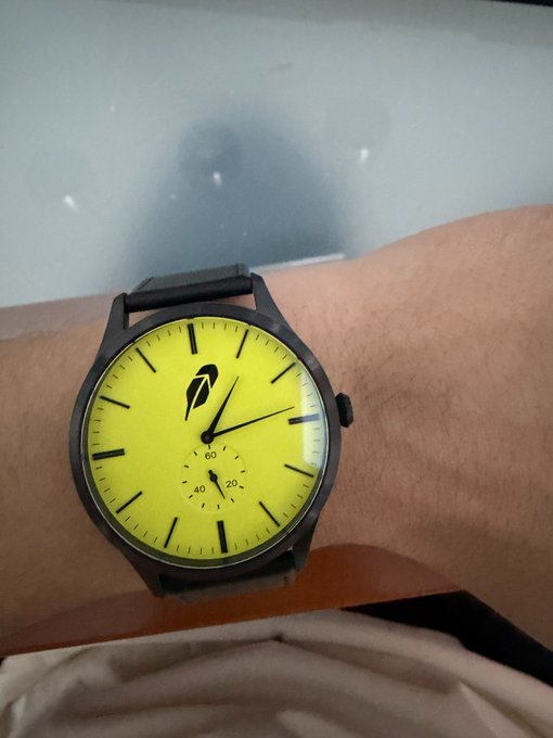 A wristwatch with a bright yellow face worn on a person's wrist, featuring black hands and the time displayed.