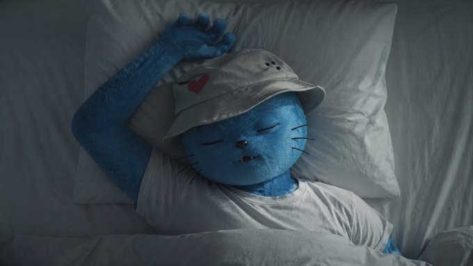 A blue Cool Cats character sleeps in a white bed wearing a bucket hat, fitting the post's mention of "@coolcats" and the casual "#gm" Thursday greeting with a tired vibe.