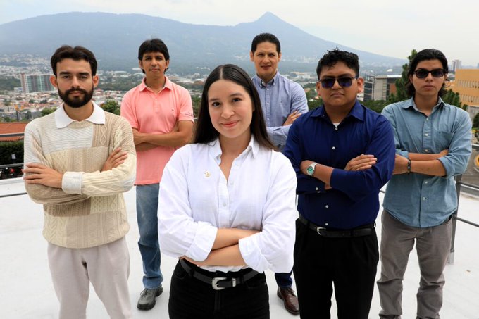 The image features a group of six young men and women standing together with their arms crossed, posing for a photo. They are all dressed similarly, wearing white shirts and black pants or skirts. The background includes mountains, suggesting that they might be on top of a building in El Salvador. The post caption reads "They said, What does a small country like El Salvador know about Bitcoin?" which implies that the group is discussing or learning about Bitcoin, possibly as part of their travels around the world and experiences.