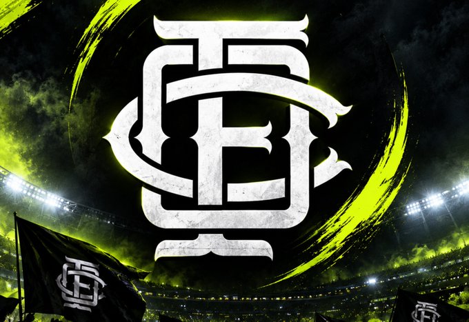 A bold stylized monogram logo featuring intertwined letters resembling "OFC" in white is centered against a dramatic stadium backdrop with green lighting and a matching flag below. The emblem reinforces the $OFC brand identity referenced in the post about upcoming token vesting claims and system improvements.