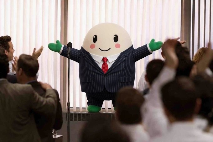 A cheerful egg-shaped mascot wearing a pinstripe suit and red tie stands triumphantly at a podium with arms outstretched, as an enthusiastic crowd cheers below, symbolizing the celebratory and meteoric rise toward the $100 million milestone referenced in the post about $CUPSEY.