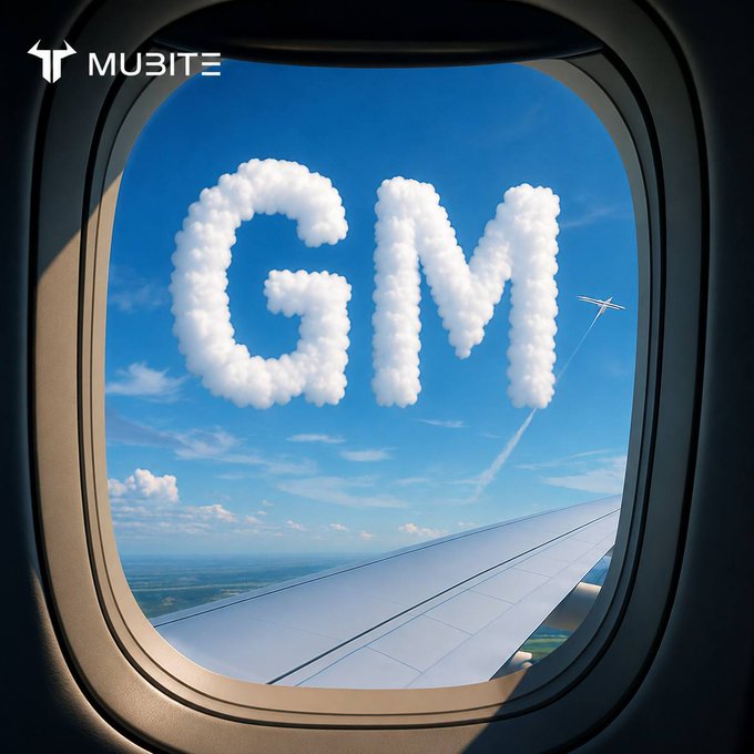A view through an airplane window showing a white airplane wing against a blue sky, with large clouds shaped into the letters 'GM' (good morning) and a smaller plane flying in the distance, with a 'MUBIT' logo in the corner.