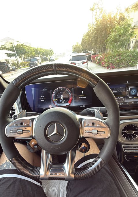 View from the driver's seat of a Mercedes-AMG, showing the carbon fiber steering wheel and digital dashboard display with the vehicle in 'Park'.