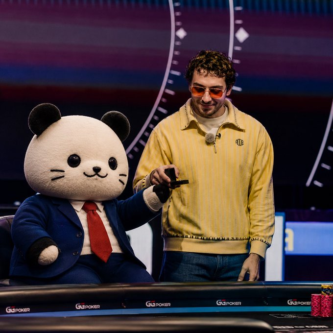 A man in a yellow striped pullover and red-tinted sunglasses stands next to a large panda mascot wearing a blue suit and red tie at a GGPoker-branded poker table.
