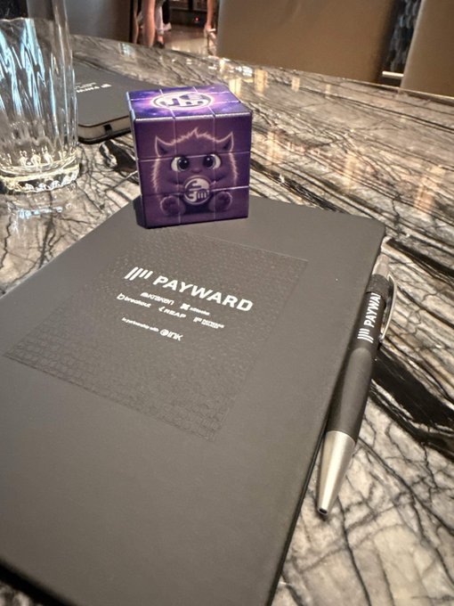 A branded 'PAYWARD' notepad, pen, and a purple cube featuring a cartoon mascot rest on a marble countertop.