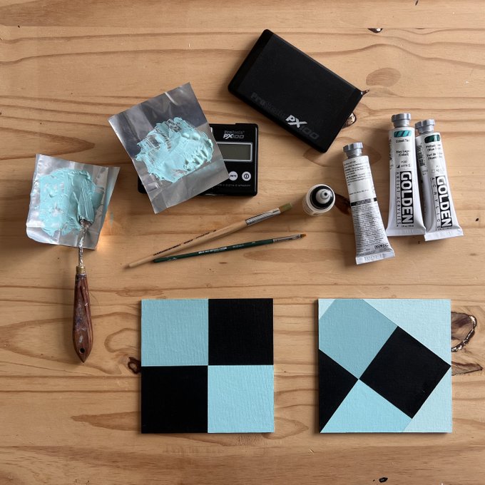 A flat lay on a wooden surface showing the tools and process of creating geometric acrylic paintings in mint green and black, with two finished checkered/rotated square canvases, Golden brand paint tubes, brushes, a palette knife, a PX100 scale, and paint-smeared foil palettes. The "Gm" caption pairs well with the artistic morning creative session depicted.