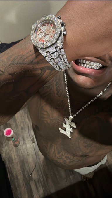 A shirtless, tattooed man flexes his arm to prominently display a fully iced-out AP-style watch and a diamond "W" pendant, paired with grills in his mouth, flexing the "champ" status he just purchased with 0.15 SOL. The post caption invites comments from viewers impressed by the flex.