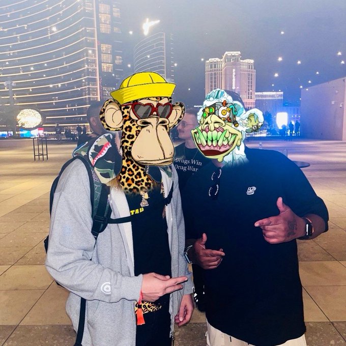 Two people posing together at night with cartoon animal face filters (a giraffe in yellow hat/heart sunglasses and a green ogre), set against an illuminated city skyline.