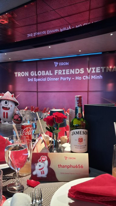 A dinner table set for the 'TRON GLOBAL FRIENDS VIETNAM 3rd Special Dinner Party - Ho Chi Minh' event, featuring a Jameson Irish Whiskey bottle, Coca-Cola, red roses, and a place card reading 'thanphu656'.