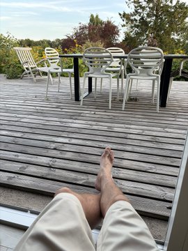 A person relaxes barefoot on a wooden deck, overlooking patio chairs and a serene outdoor view, capturing a peaceful moment of reflection that echoes the post's message of calm acceptance regarding SPX6900.