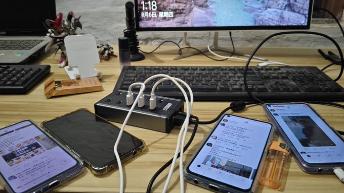 A wooden desk holds a multi-port USB hub, three smartphones displaying various screens, a keyboard, and a computer monitor showing a snowy landscape and the date '6月6日'.