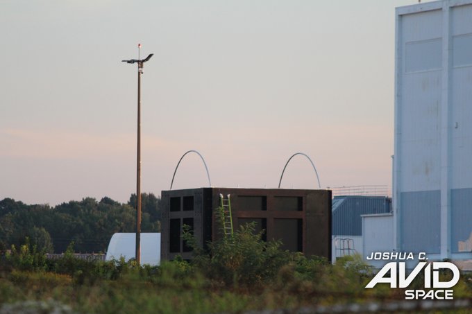 A landscape photograph at dusk showing industrial structures and a bird perched on a pole, with a watermark reading "JOSHUA C. AVID SPACE".