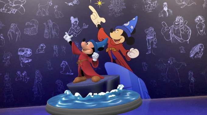 Mickey and Minnie Mouse as Sorcerer's Apprentice figures (from Fantasia) in red robes and blue wizard hats with arms raised, displayed on a rocky base with blue wave effects against a dark blue background covered in character sketches.