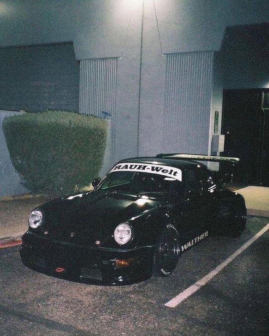 A black Porsche 911 with "RAUH-Welt" on the windshield and "WALTHER" on the side parked at night.