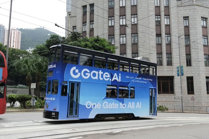 A blue double-decker tram in Hong Kong with advertising for 'Gate.AI' ('One Gate to All AI') and 'Photo Routing', traveling past a building with mountains in the background.