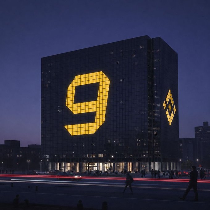 A modern glass office building at dusk with a large illuminated yellow '9' (likely Binance) displayed on its facade, with people and light trails visible on the street below.