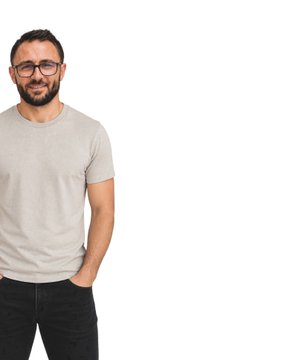 A man with glasses, a beard, and a gray t-shirt smiles at the camera, standing on the left side of a blank white background.