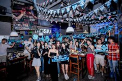 A group of people pose together at a lively Bitget World Cup Shenzhen offline event, with the "Bitget" logo prominently displayed on a sign behind them, matching the post about enjoying craft beer and a great atmosphere.