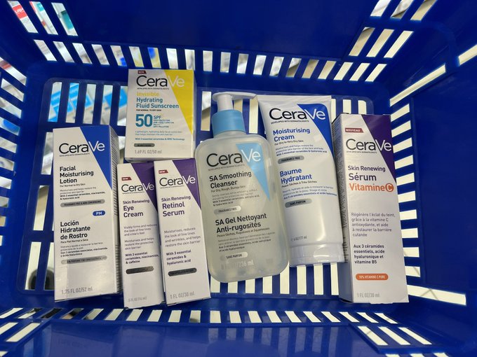 Blue shopping basket containing various CeraVe skincare products including Hydrating Fluid Sunscreen SPF 50, Facial Moisturising Lotion, SA Smoothing Cleanser, Moisturising Cream, and Skin Renewing Serum with Vitamin C.